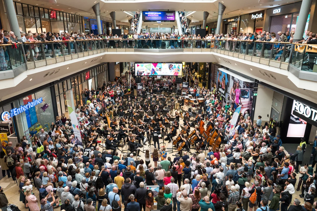 The full City of Birmingham Symphony Orchestra plays to a large crowd gathered on the ground floor and the balconies of the Bullring shopping centre.