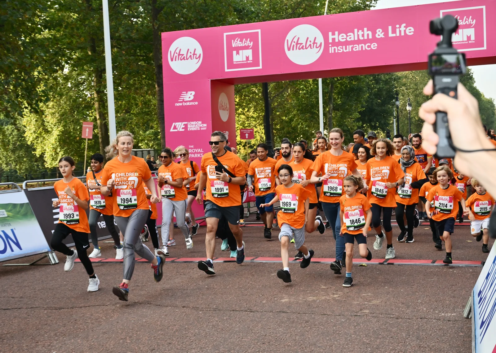 Children and adults wearing orange Children with Cancer UK shirts set off beneath the pink Westminster Mile start arch at a previous year's event.